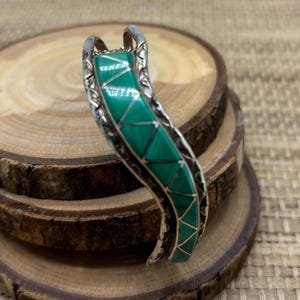 May include: A silver and green turquoise bracelet with a wavy design. The bracelet is made of sterling silver and features a green turquoise inlay.