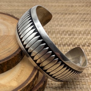 May include: A wide silver cuff bracelet featuring a repeating pattern of raised, elongated oval shapes separated by dark, recessed grooves. The interior of the metal band is stamped with the text B. WEBB.