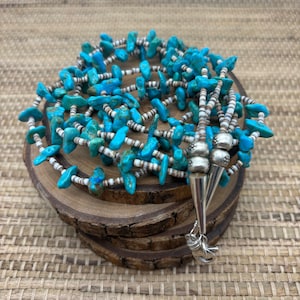 May include: A turquoise and white beaded necklace with silver accents. The necklace is made of turquoise stones and white beads, and it has a silver clasp.