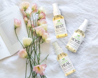May include: Three glass bottles with spray tops containing essential oil blends. The bottles are labeled "Clearly Rest", "Clearly Mood", and "Clearly Heal". Each bottle has a green leaf logo and text describing the aromatherapy benefits of the blend.