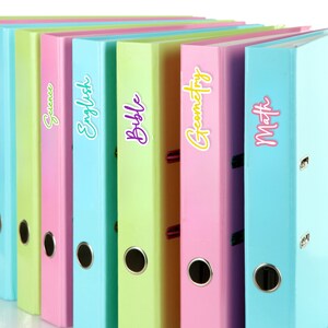 May include: A row of colorful binders in pastel shades of green, pink, and blue. Each binder is labeled with a subject: Science, English, Bible, Geometry, and Math. The binders are arranged in a neat row.