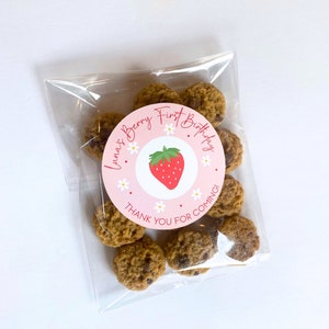 K&ouml;nnte beinhalten: Ein klarer Zellophanbeutel gef&uuml;llt mit Schokoladen-Chip-Cookies. Ein runder Aufkleber auf dem Beutel tr&auml;gt die Aufschrift "Luna's Berry First Birthday" mit einer Erdbeerillustration und den Worten "Thank You For Coming!"