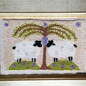 Op de afbeelding: Een ingelijst naaldkunstwerk met twee witte schapen die onder een treurwilg staan met een paars hart. De achtergrond is crèmekleurig met groen gras en paarse bloemen.