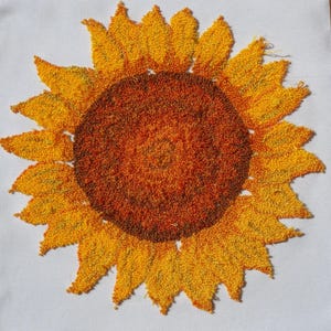 May include: A close-up of a yellow and orange embroidered sunflower. The sunflower is made of yarn and has a textured, fuzzy appearance.