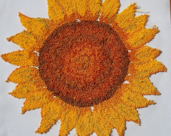 May include: A close-up of a yellow and orange embroidered sunflower. The sunflower is made of yarn and has a textured, fuzzy appearance.