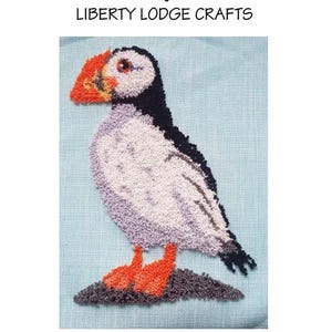 May include: A punch needle pattern featuring a colorful puffin bird design. The bird has a black back, white belly, and orange beak and feet. The text "PUFFIN" and "PUNCH NEEDLE PATTERN" are at the top. The Etsy shop name is also included.