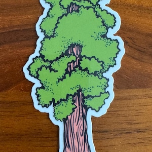 May include: A sticker featuring a stylized illustration of a redwood tree. The tree has a pinkish-brown trunk with black lines and layers of green foliage. The sticker has a white border and is on a wooden surface.