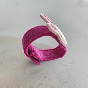 Puede incluir: Una pulsera de fieltro rosa con un dise&ntilde;o de flor de fieltro blanco y rosa.