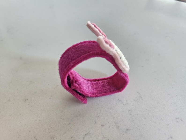 Puede incluir: Una pulsera de fieltro rosa con un dise&ntilde;o de flor de fieltro blanco y rosa.