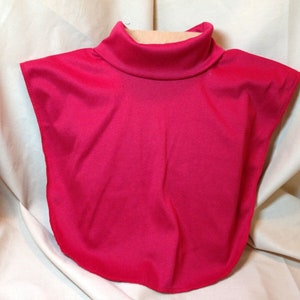 Op de afbeelding: Een fel fuchsia kleurige coltrui kraag. De kraag is gemaakt van een gladde, mogelijk satijnachtige stof. Het ontwerp omvat een hoge, afgeronde halslijn en strekt zich uit over de schouders en biedt een stijlvolle layering optie.
