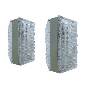May include: A pair of rectangular wall sconces featuring clear, textured glass panels with a repeating bubble pattern. Each light fixture is centered with a vertical, smooth, light gray metal strip that runs the full height of the glass.