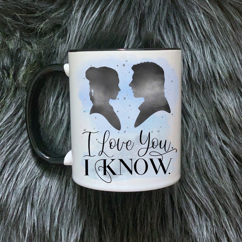 Może przedstawiać: Biały kubek ceramiczny z czarnym uchwytem. Kubek ma niebieskie tło akwarelowe z sylwetkami mężczyzny i kobiety. Tekst "I love you, I know." jest nadrukowany czarnym, ozdobnym pismem.