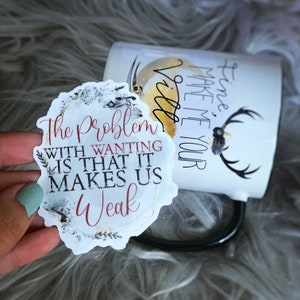 May include: A white ceramic mug with black text that reads "Time, Make Me Your Vill". A white sticker with black and grey watercolour-style background and gold accents reads "The Problem With Wanting Is That It Makes Us Weak".
