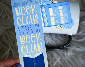 May include: A blue and yellow bookmark with the text "What happens in book club stays in book club". The bookmark features a blue book with a white spine and a yellow flower design.