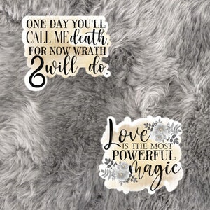 May include: Two watercolor-style stickers with inspirational quotes. The first sticker is beige with black text that reads "One day you'll call me death. For now wrath will do." The second sticker is beige with black text that reads "Love is the most powerful magic." The sticker has a floral design with gray flowers and leaves.