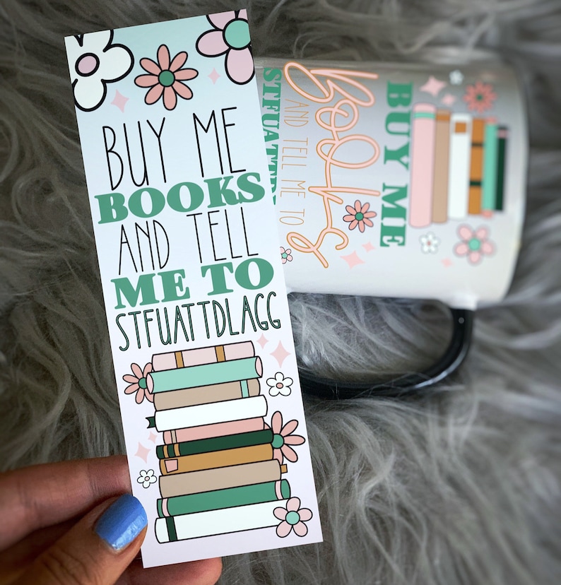 May include: A pink and green bookmark with a stack of books and the text "BUY ME BOOKS AND TELL ME TO STFUATTDLAGG".