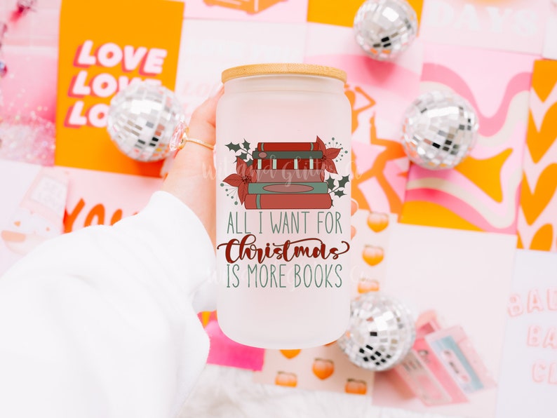 May include: A white frosted glass mug with a bamboo lid. The mug has a graphic of a stack of books with a red poinsettia and holly. The text reads "All I want for Christmas is more books".