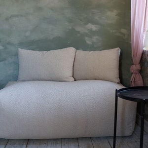 Könnte beinhalten: Ein weißes, gestepptes, modulares Sofa mit zwei Kissen steht vor einer grünen Wand mit einem rosa Vorhang und einem schwarzen Beistelltisch.