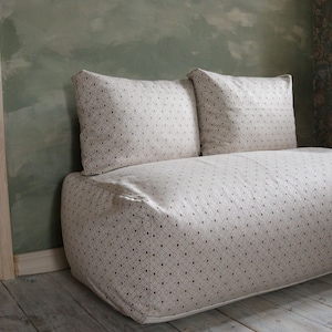 May include: A white and beige patterned sofa with two matching pillows. The sofa is made of a soft, plush fabric and has a simple, modern design.