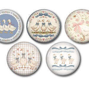 May include: A set of five circular pinback buttons featuring illustrations of white geese with blue and pink bows. The designs include groups of geese, floral patterns, gingham backgrounds, and decorative borders in shades of blue, pink, and cream.