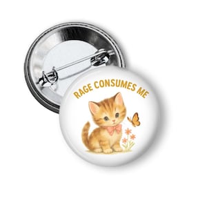 May include: A white button featuring a cute cartoon orange tabby kitten wearing a pink bow tie and looking at a butterfly. The text "RAGE CONSUMES ME" is written in gold letters around the kitten.