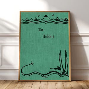 Puede incluir: Una lámina decorativa rectangular con un fondo verde texturizado. El texto 'The Hobbit' está impreso en negro en el centro. Sobre el texto hay una ilustración negra de montañas y debajo un dibujo de líneas negras de un dragón.