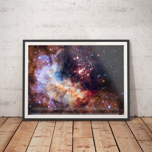 May include: A framed photograph of a colorful nebula with a cluster of stars in the center. The nebula is a mix of pink, orange, blue, and purple hues, with a dark background of stars.