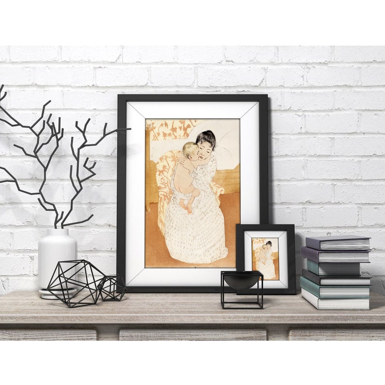 Op de afbeelding: Een ingelijste print van een schilderij dat een vrouw afbeeldt die een kind in haar armen houdt. De vrouw draagt een witte jurk met een bloemenpatroon en het kind draagt een witte jurk. Het schilderij is geplaatst tegen een lichtbruine achtergrond.