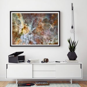 K&ouml;nnte beinhalten: Ein gerahmtes Foto eines Nebels im Weltraum, mit wirbelnden Wolken aus Gas und Staub in Rot-, Orange-, Gelb- und Blaut&ouml;nen. Das Foto h&auml;ngt an einer wei&szlig;en Wand &uuml;ber einer wei&szlig;en Medienkonsole mit einem schwarzen Plattenspieler, Kopfh&ouml;rern und B&uuml;chern.