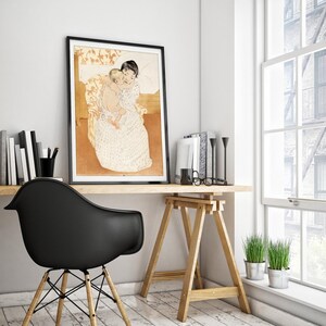 Op de afbeelding: Een zwart ingelijste print van een schilderij dat een vrouw afbeeldt die een kind in haar armen houdt. De vrouw draagt een witte jurk met een bloemenpatroon en het kind draagt een witte luier. Het schilderij is geplaatst tegen een lichtbruine achtergrond.