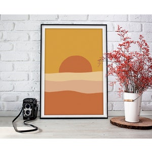 May include: A framed print of a minimalist sunset landscape with a yellow, orange, and brown color scheme. The sun is a large orange circle above a series of wavy lines representing the horizon.
