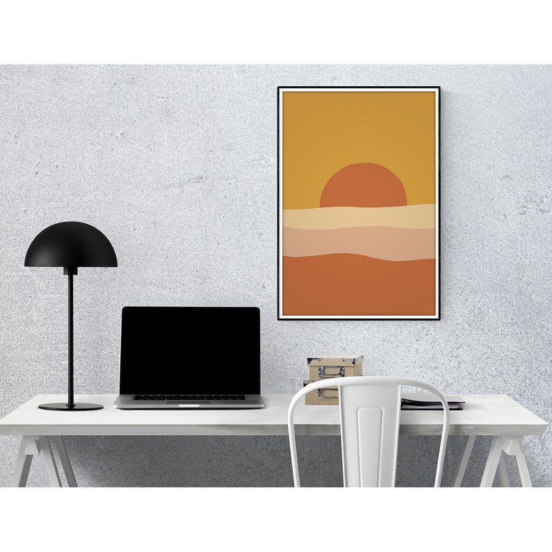 May include: A minimalist abstract art print with a sunset over a landscape in shades of orange, yellow, and brown. The print is framed in black and is hanging on a gray wall.
