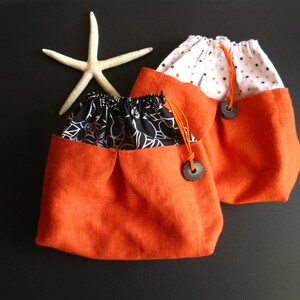 May include: Two orange drawstring bags with black and white floral fabric lining. One bag has a white background with pink polka dots.