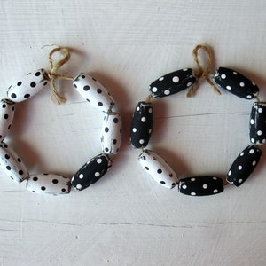 May include: Two black and white polka dot wreaths made of wooden beads tied together with twine.