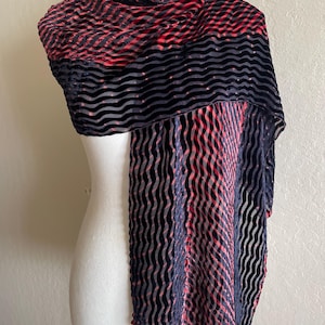 May include: A rectangular scarf featuring a textured, wavy pattern in alternating black and deep red. The fabric displays a distinct raised velvet-like finish with a repeating horizontal and vertical ripple design that creates a visual depth.