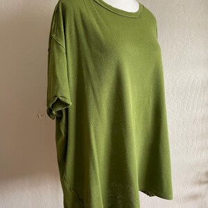 May include: Olive green short-sleeved t-shirt with a round neckline. The shirt has a relaxed fit and a textured appearance. The seams have a raw edge detail, adding a casual touch to the garment.