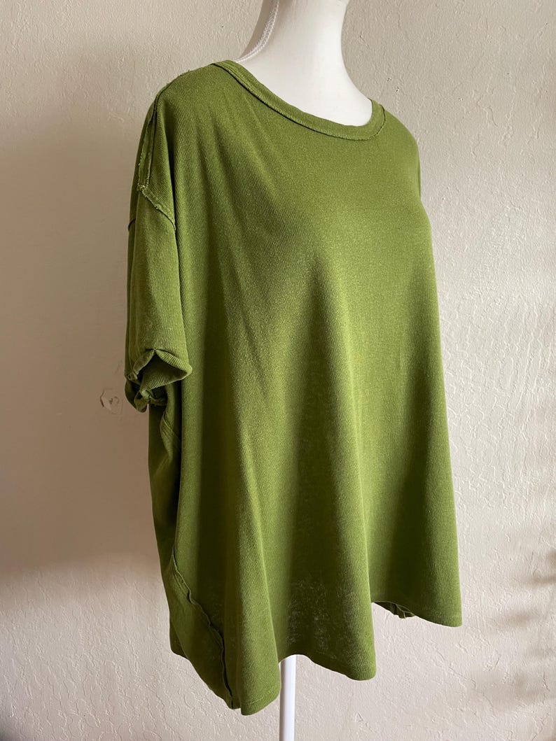 May include: Olive green short-sleeved t-shirt with a round neckline. The shirt has a relaxed fit and a textured appearance. The seams have a raw edge detail, adding a casual touch to the garment.