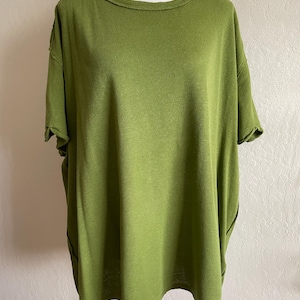 May include: Olive green short-sleeved top with a round neckline. The shirt has a loose, oversized fit and a slightly textured appearance. The sleeves are cuffed, and the fabric appears to be a soft knit material. The top is displayed on a mannequin.