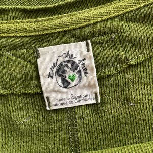 May include: Close-up of a green ribbed knit top with a crew neck. A white tag is sewn on the garment, featuring a globe with a green heart and the words "we the free". The tag also reads "made in Cambodia" and "fabriqu&eacute; au Cambodge".