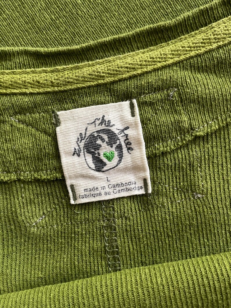 May include: Close-up of a green ribbed knit top with a crew neck. A white tag is sewn on the garment, featuring a globe with a green heart and the words "we the free". The tag also reads "made in Cambodia" and "fabriqu&eacute; au Cambodge".