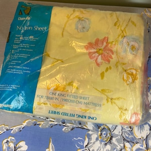 May include: A yellow fitted sheet with a floral pattern in shades of pink, blue, and green. The sheet is packaged in plastic and labeled "One King Fitted Sheet for 78x80 in. (198x203 cm) Mattress".
