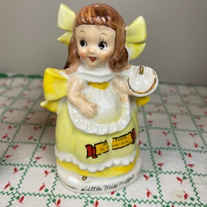 K&ouml;nnte beinhalten: Eine Porzellanfigur eines M&auml;dchens in einem gelben Kleid und einer gelben Schleife im Haar. Sie h&auml;lt ein Hufeisen in der Hand. Die Figur ist mit "Silver Beach St. Joseph Mich." und "Little Miss Muffet" beschriftet.