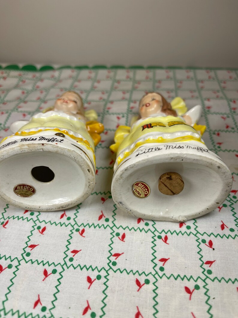 K&ouml;nnte beinhalten: Ein Paar vintage Salz- und Pfefferstreuer mit Little Miss Muffet. Die Streuer sind aus Keramik und in Gelb, Wei&szlig; und Rot bemalt. Auf der Unterseite jedes Streuers befindet sich ein Aufkleber mit der Aufschrift "Relco, Handcrafted, Japan".