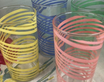 May include: Four clear glass drinking glasses with colorful striped designs. The glasses have yellow, blue, green, and pink stripes.
