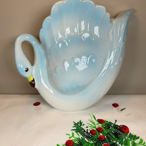 May include: A blue and white ceramic swan shaped dish. The swan has a raised tail and a detailed head with a yellow beak.