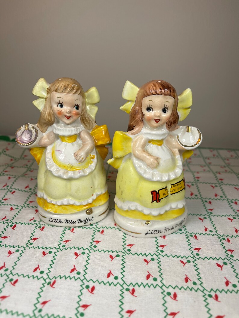 K&ouml;nnte beinhalten: Ein Paar antike Salz- und Pfefferstreuer aus Keramik mit Little Miss Muffet. Die Streuer sind gelb und wei&szlig; mit einer gelben Schleife und einem gelben Kleid. Die Streuer halten eine Sch&uuml;ssel mit Quark und Molke und einen L&ouml;ffel.