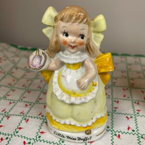 K&ouml;nnte beinhalten: Eine Porzellanfigur von Little Miss Muffet, einem M&auml;dchen in einem gelben Kleid und einer Sch&uuml;rze, das eine Sch&uuml;ssel und einen L&ouml;ffel h&auml;lt. Die Figur steht auf einem wei&szlig;en Hintergrund mit einem roten und gr&uuml;nen Muster.