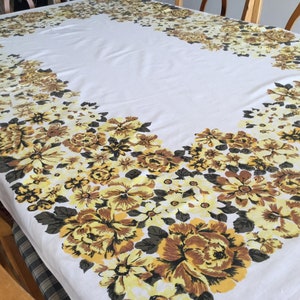 May include: White tablecloth with a yellow and brown floral border. The flowers are large and have a vintage style.