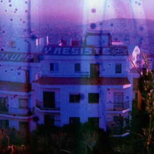 May include: A purple and blue image of a building with the words "OKUPA Y RESISTE" painted on the side. The building is surrounded by trees and bushes.