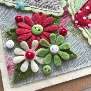 May include: Handmade greeting card with felt flower embellishments. Features red, white, and green felt flowers with button centres. The number "4" is appliqu&eacute;d in red with white polka dots. The card has a neutral colour palette.